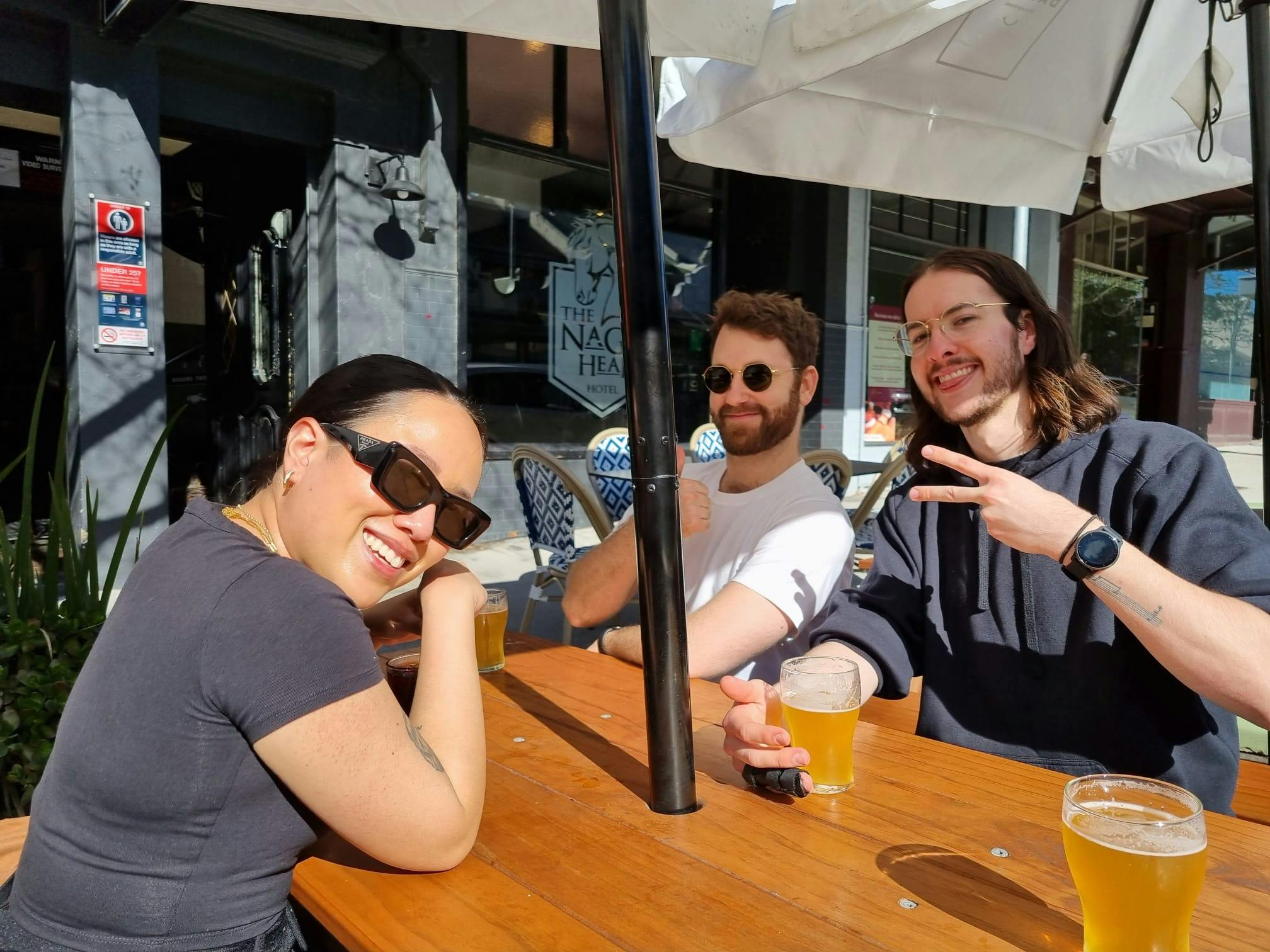 Greg, Annisa and Aaron smiling and having a beer in the sunshine